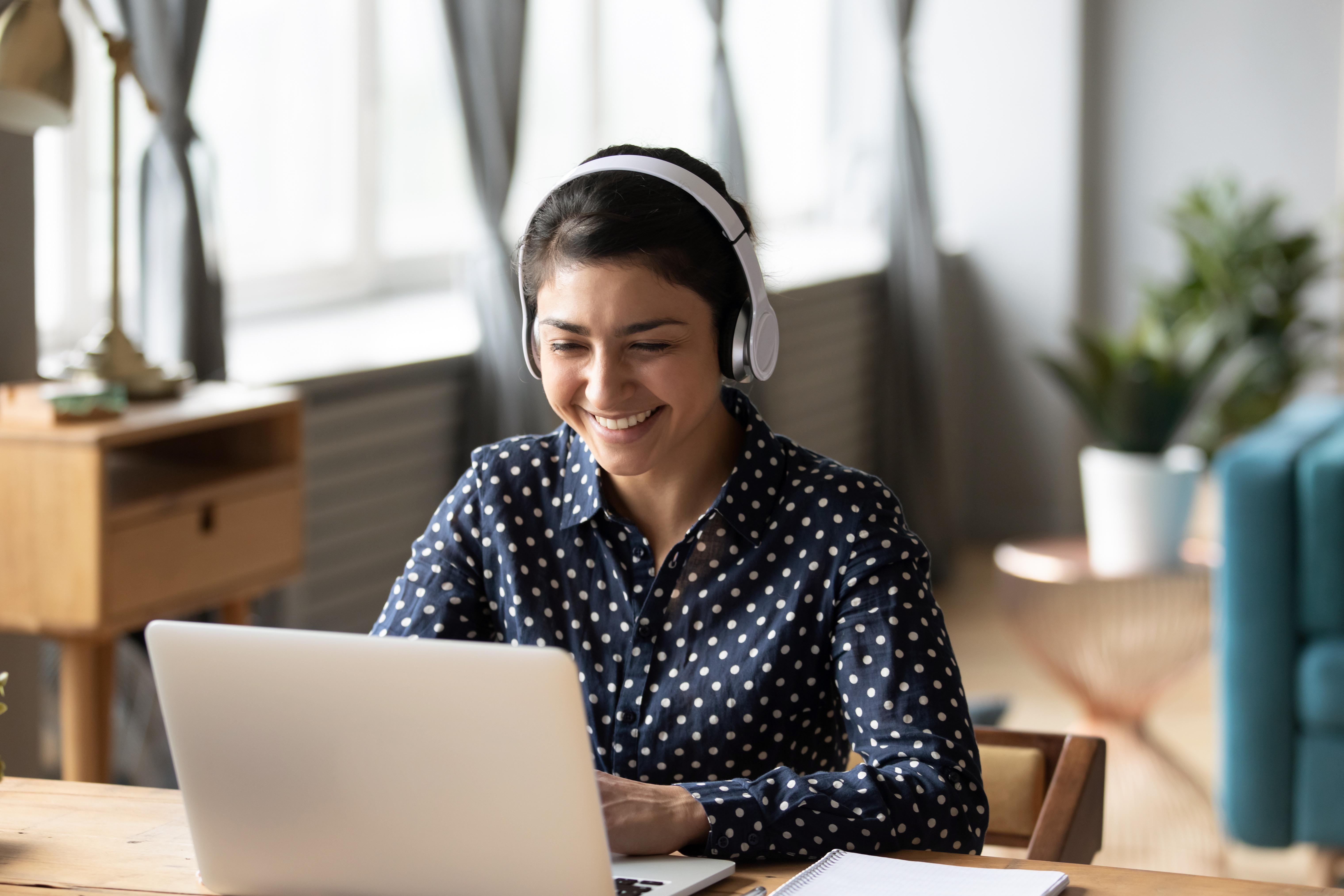 Person sits at desk, wearing headphones and smiling.
