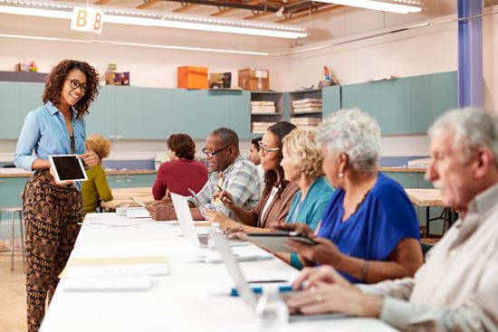 Instructor stands in a classroom, addressing a room of adults.