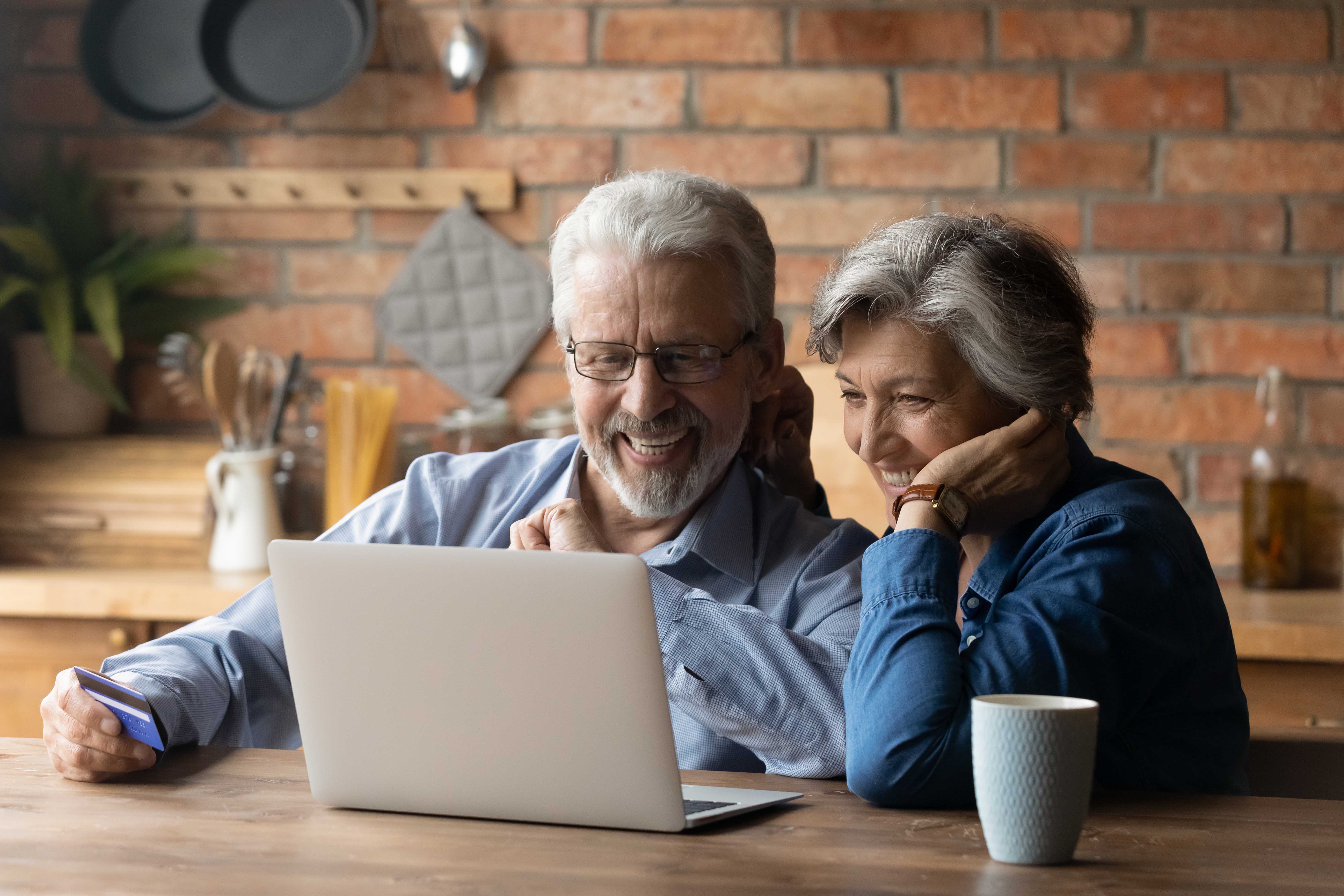 Two seniors sit at a table and laptop, smiling.