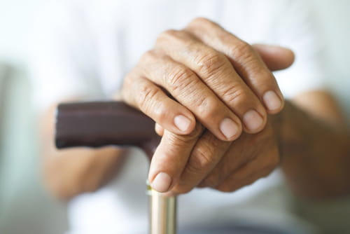 Close-up of senior's hands resting on a walking cane.