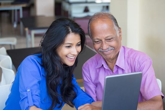 A senior and a younger person use a laptop together.